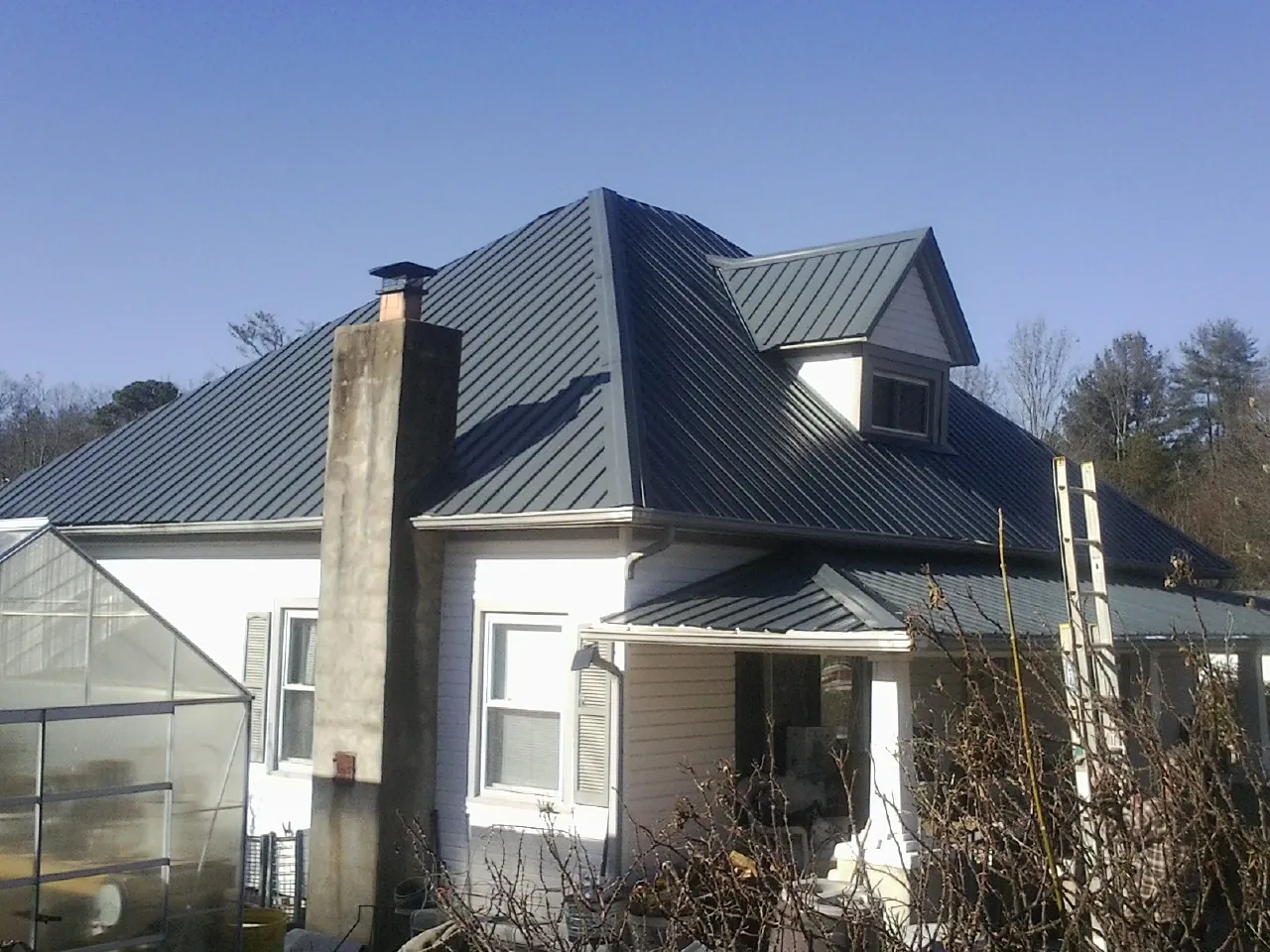 Dark blue standing seam metal roof on a white farmhouse with dormer — Slate & Tile Roof Repair by Roofing Brothers in Joffre