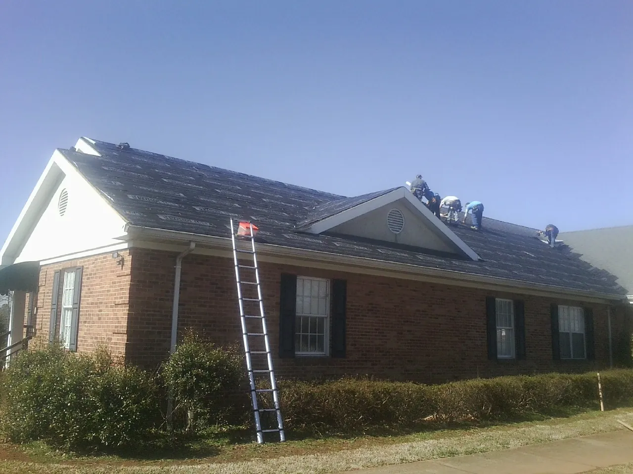 Crew tearing shingles off a brick ranch roof with a ladder set — Emergency Roof Repair work by our crew in Joffre