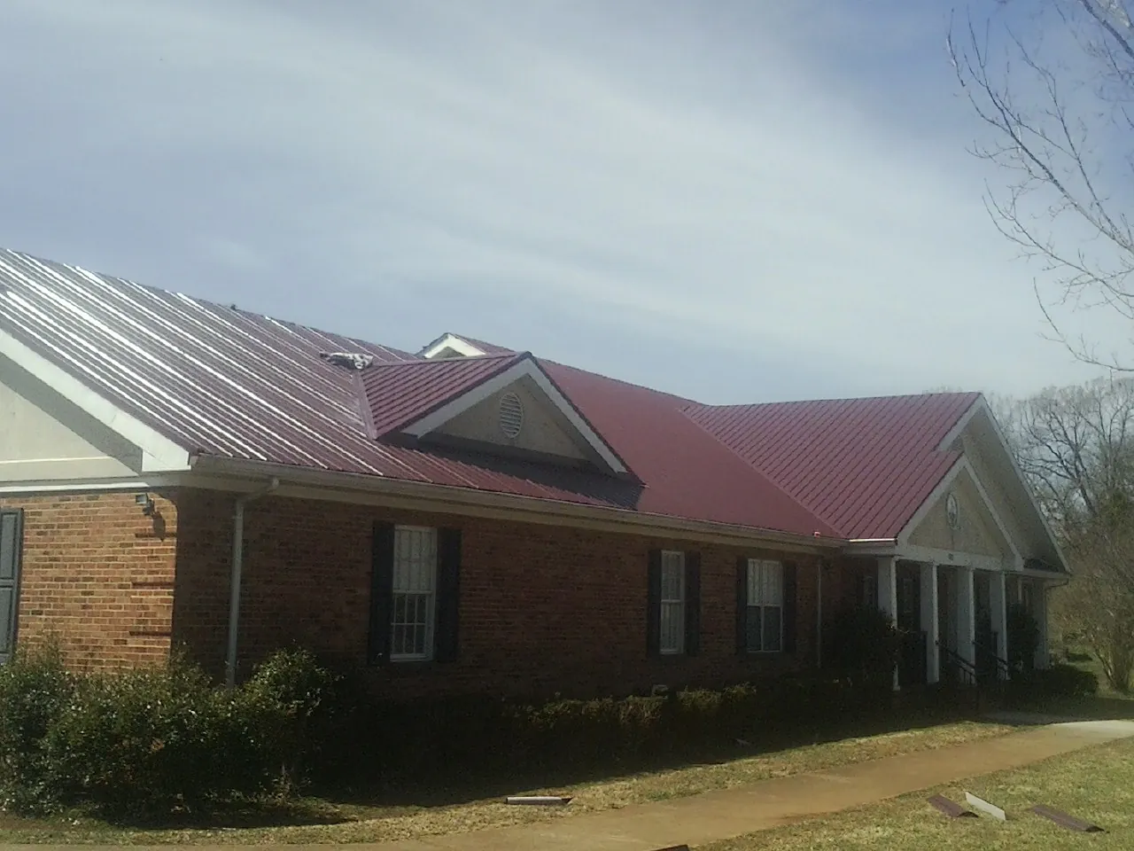 Red metal roof with gabled entries on a long brick building, from a Hail Damage Roof Repair job in Joffre