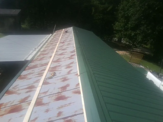 Old rusted panels beside newly installed green metal roofing — Wind Damage Roof Repair by Roofing Brothers in Joffre