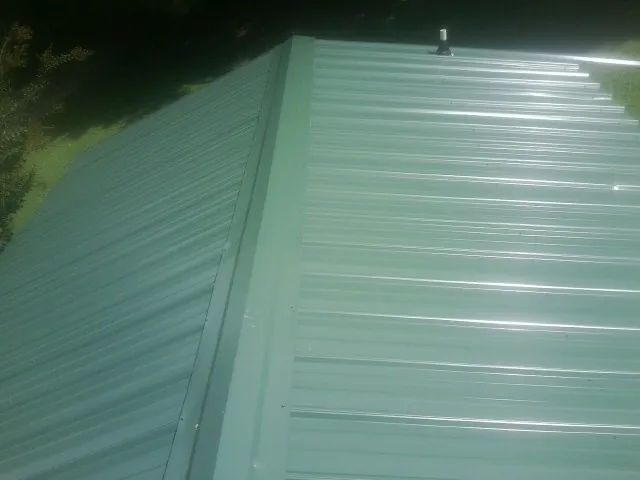 New green metal panels meeting at the ridge of a roof — Flat Roof Repair work by our crew in Joffre