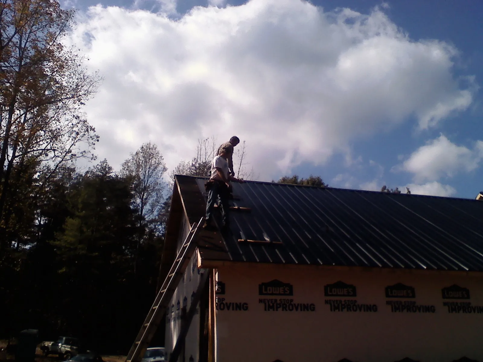Roofer fastening dark metal panels high against a cloudy sky, from a Roof Inspection job in Joffre