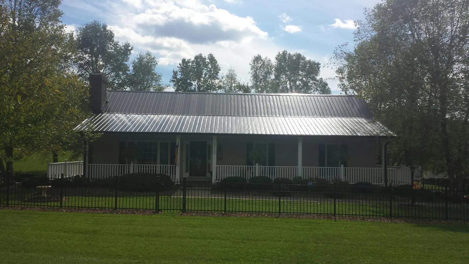 Gray metal roof on a brick ranch with a full width front porch — Gutter Guard Installation work by our crew in Joffre