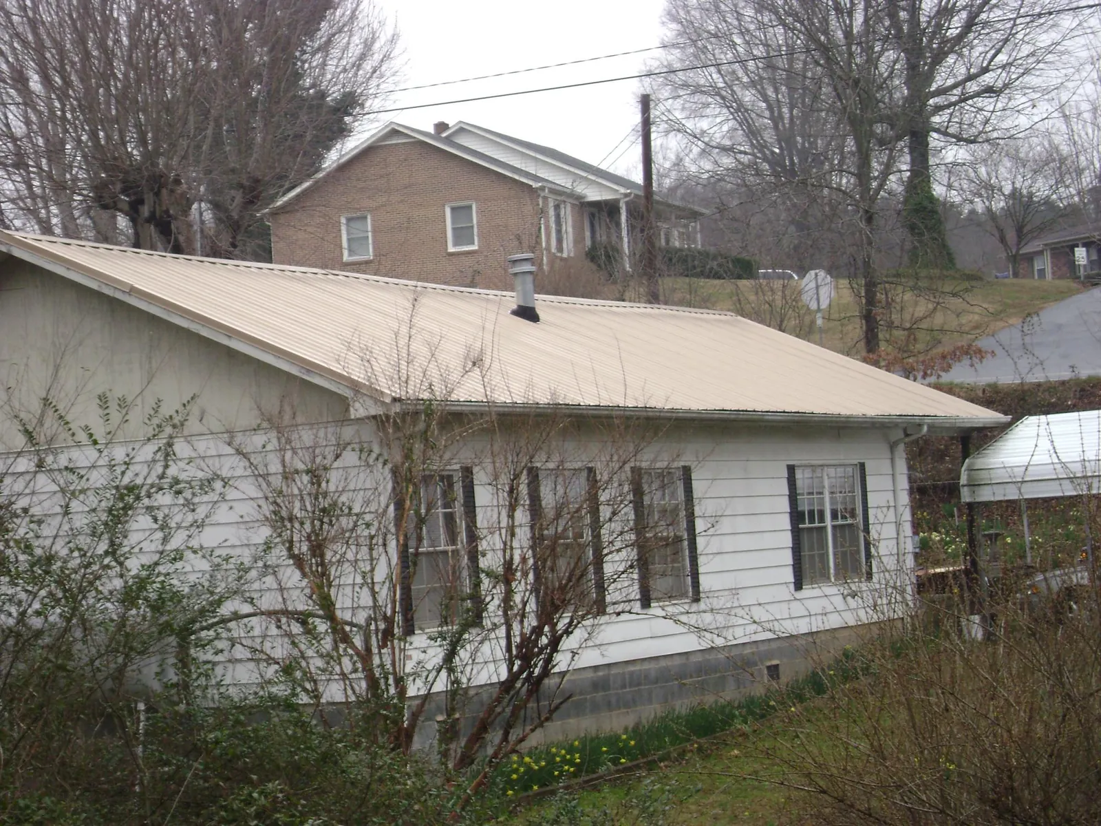 Tan metal roof on a white sided house set into a hillside — Commercial Roofing by Roofing Brothers in Joffre