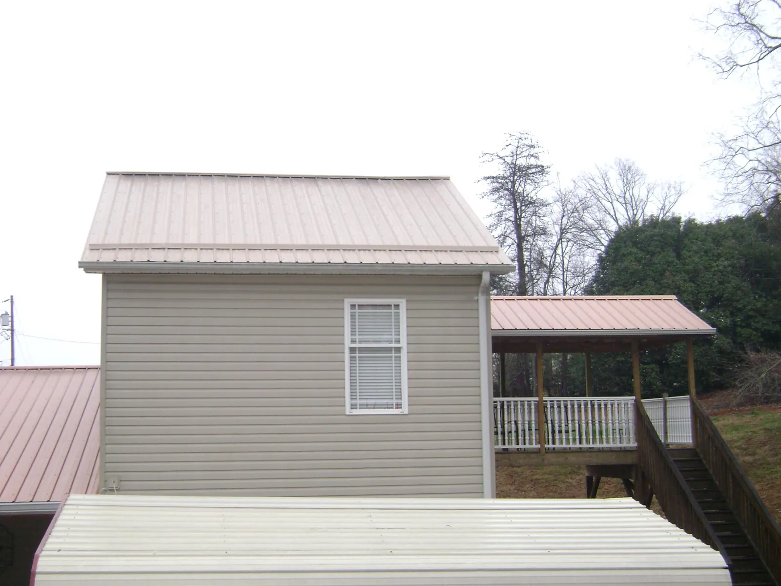 Tan metal roofs on a two story addition and attached porch, from a Roof Replacement job in Joffre